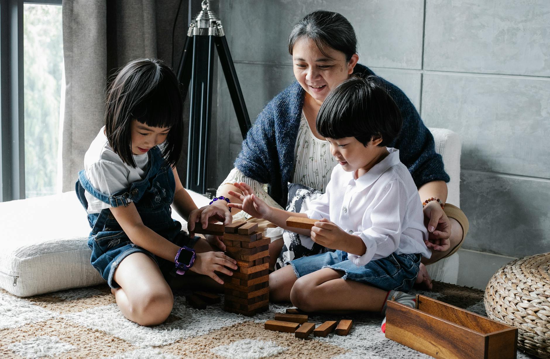 cheerful little ethnic siblings playing board game with help of smiling grandmother